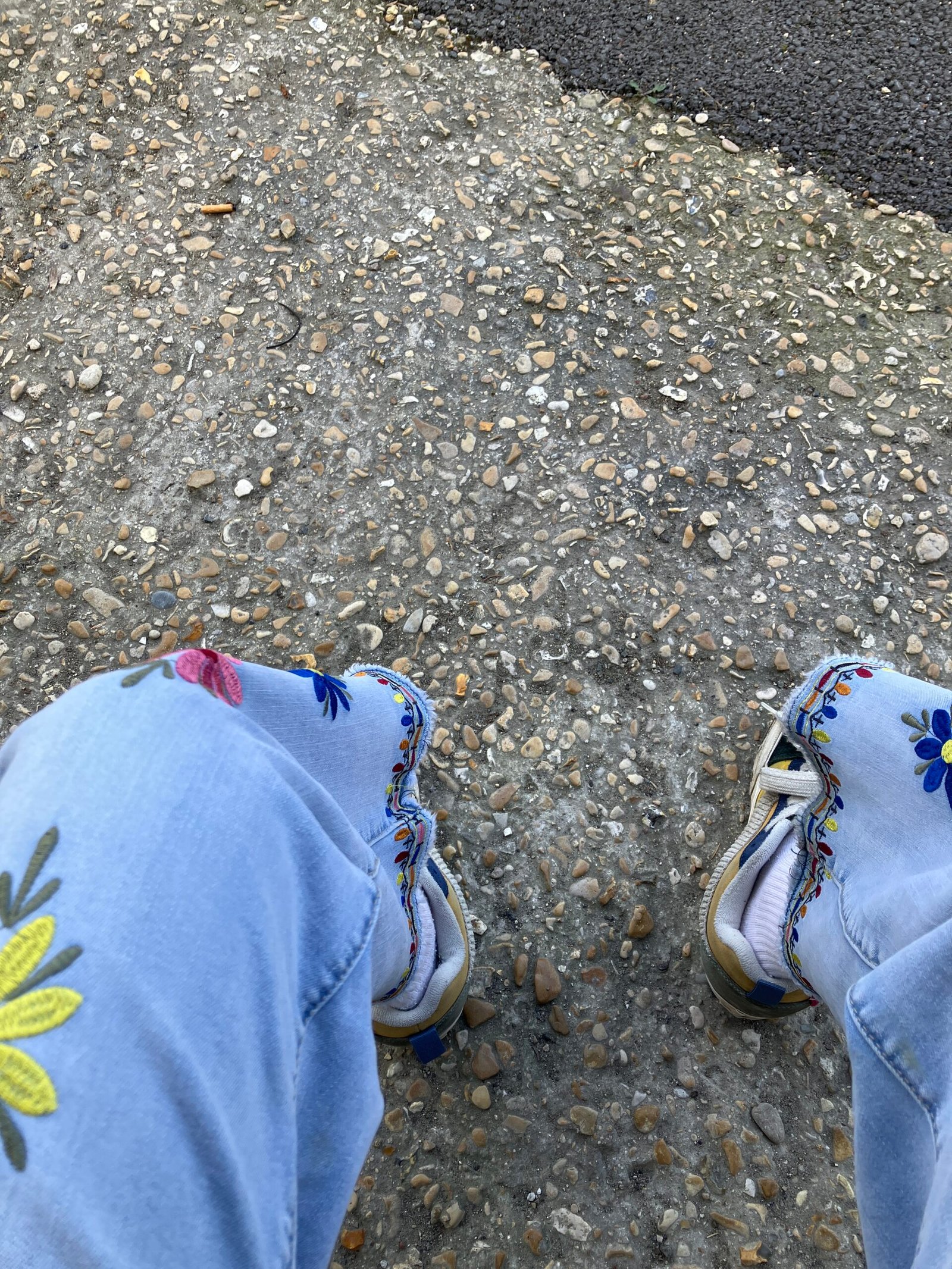Vue du dessus — jean brodé de fleurs, chaussures brodées multicolores sur gravier — Villevaude avril 2025