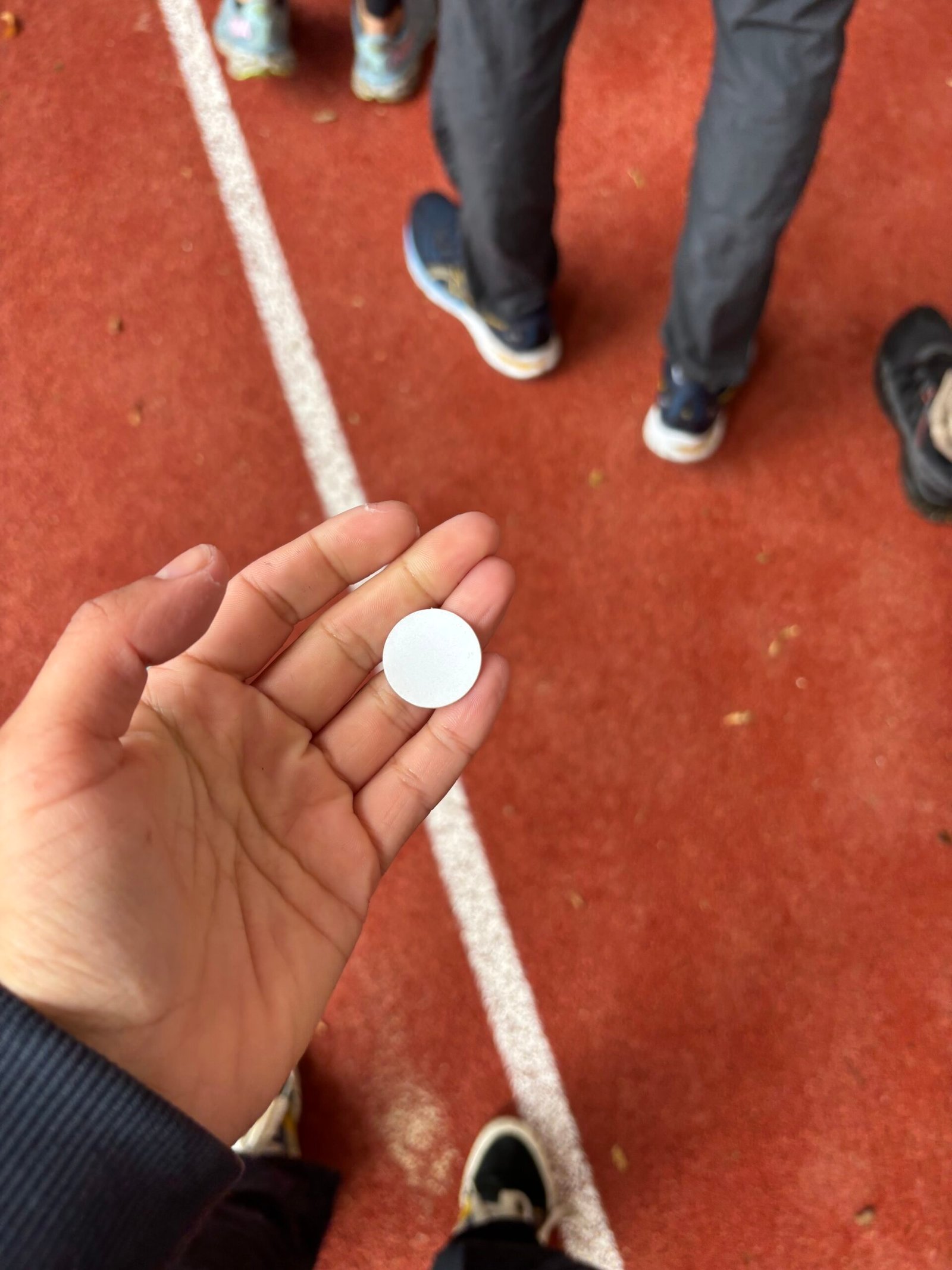 Jeton blanc de la Ligue contre le cancer dans une paume ouverte, piste d'athlétisme rouge en arrière-plan — Relais pour la Vie du Nord 2026